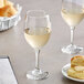 Two Acopa wine glasses filled with white wine on a table next to a plate of bread.