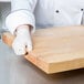 A person wearing gloves holding a Choice wood cutting board.