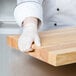 A person wearing white gloves holding a Choice wood cutting board.