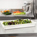 A white Cambro food pan filled with salad on a counter.