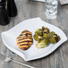 A white Elite Global Solutions irregular square melamine platter with grilled chicken and brussels sprouts on it.