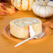 A slice of roll cake with cream cheese frosting on a pumpkin spice orange paper plate.