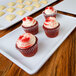 A white rectangular melamine tray with red velvet cupcakes with white frosting and red sprinkles.