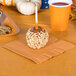 A caramel apple with nuts on a Pumpkin Spice Orange luncheon napkin next to a cup of red liquid.