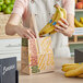 A person holding bananas in a Choice natural brown kraft paper bag with a yellow and green "Go Bananas - Sophomore" label.
