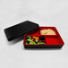The black and red rectangular lid for a black Elite Global Solutions bento box with rice, broccoli, and carrots inside.