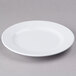A white Elite Global Solutions round melamine platter with a rim on a gray surface.