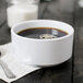 A white Elite Global Solutions melamine cup filled with coffee on a table with a napkin and a spoon.