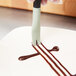 A hand using a Mercer Culinary square notch plating tool to drizzle chocolate syrup on a plate.