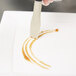 A hand using a white Mercer Culinary silicone brush to plate brown liquid.