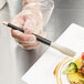 A hand using a Mercer Culinary silicone brush to plate food.