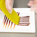 A person using a yellow Mercer Culinary silicone plating tool to place chocolate syrup on a white plate.