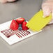 A person using a Mercer Culinary silicone wedge plating tool to place fruit on a plate.