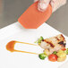 A hand holding a Mercer Culinary silicone wedge plating tool over a plate of food.