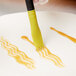 A hand using a yellow Mercer Culinary silicone brush to add brown liquid to a white plate.