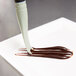 A Mercer Culinary square notch silicone brush dripping chocolate onto a white plate.