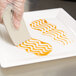 A person's hand in a plastic glove using a Mercer Culinary round arch silicone wedge to plate orange sauce.