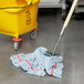 A Rubbermaid wet mop with a wooden handle in a blue mop bucket.