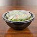 A black Sabert round bowl filled with salad on a table.