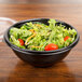 A close up of a salad in a black Sabert round bowl.