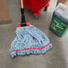 A Rubbermaid Blue Large Web Foot Shrinkless Blend Mop Head on the floor next to a bucket.