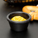 A black Carlisle ramekin filled with yellow mustard on a table with pretzels.