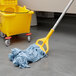 A blue Rubbermaid wet mop on the floor next to a yellow mop bucket.