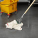 A Rubbermaid white blend wet mop with a wooden handle in a yellow bucket.
