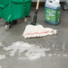 A Rubbermaid white blend wet mop in a green bucket of soapy liquid on the floor.