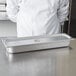 A chef in a white coat standing in front of a stainless steel Choice half size long pan cover.