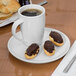A cup of coffee and pastries on a white Libbey porcelain saucer.