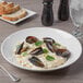 A Libbey Royal Rideau white porcelain bowl filled with pasta, mussels, and basil leaves.