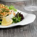 A Libbey white porcelain platter with food including a piece of fish and a lemon wedge on it.