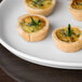 A white Libbey oval porcelain tray with small quiches topped with greenery.