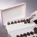 A gloved hand picking chocolates out of a Valentine's Day heart candy box.