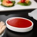 A hand holding a Libbey white porcelain oval bowl of red sauce over a plate of shrimp.