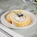 A Tuxton Hampshire eggshell embossed china bread and butter plate with a slice of cake topped with blueberries and lemon slices on a table.