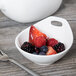 A Libbey white porcelain bowl filled with berries on a table with a fork.