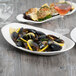A white Libbey porcelain platter of mussels with lemon slices on a table.
