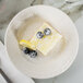 A Tuxton Hampshire Eggshell china bread and butter plate with a lemon and blueberry dessert and powdered sugar.