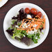 A Libbey white porcelain plate with a salad including lettuce, tomatoes, carrots, and cheese.