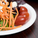 A Libbey round white porcelain plate with salad, tomatoes, and carrots.
