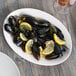 A white Libbey oval porcelain platter with mussels and lemon wedges.