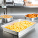 A stainless steel counter with several Durable Packaging aluminum foil pans of food.