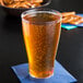 A Fineline clear plastic beer glass filled with beer on a blue napkin next to pretzels.