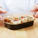 A person holding a Durable Packaging black and gold mini foil entree container filled with sushi.
