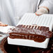 A person using gloves and a knife to spread chocolate into a Martellato chocolate mold.