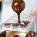 A person using a Matfer Bourgeat chocolate mold to pour liquid chocolate into half spheres.