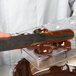 A person using a knife to cut chocolate on a Matfer Bourgeat plastic chocolate mold.