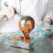 A person using a spoon to pour chocolate into a Matfer Bourgeat polycarbonate mold.